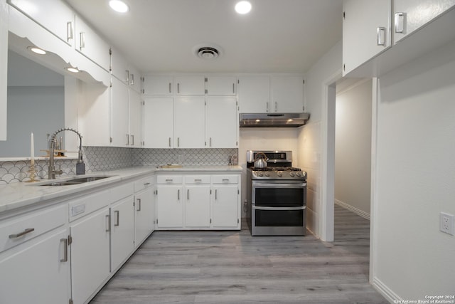 kitchen featuring double oven range, tasteful backsplash, under cabinet range hood, a sink, and visible vents