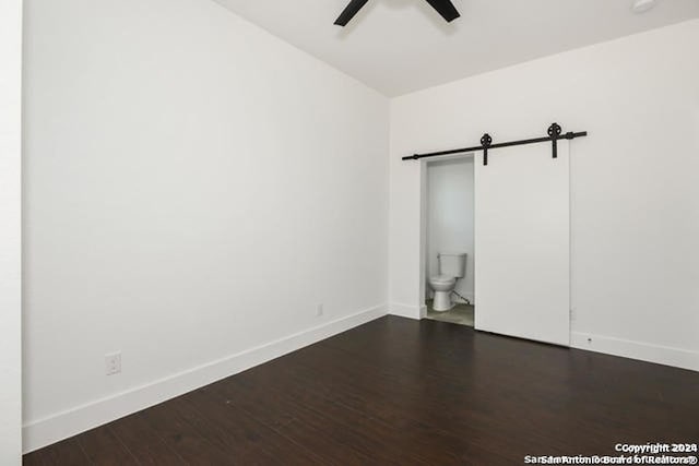 spare room featuring a barn door, ceiling fan, and dark wood-type flooring