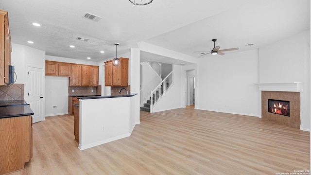 kitchen with ceiling fan, hanging light fixtures, backsplash, light hardwood / wood-style floors, and a tiled fireplace