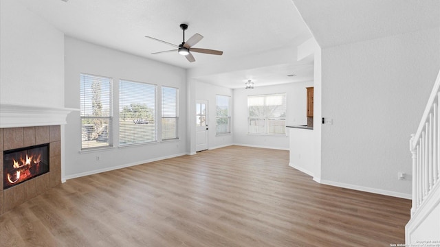 unfurnished living room with light wood-type flooring, ceiling fan, and a tiled fireplace