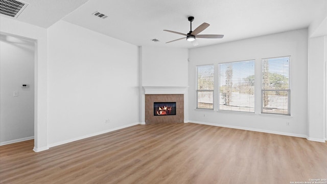 unfurnished living room featuring light hardwood / wood-style flooring, ceiling fan, and a tiled fireplace