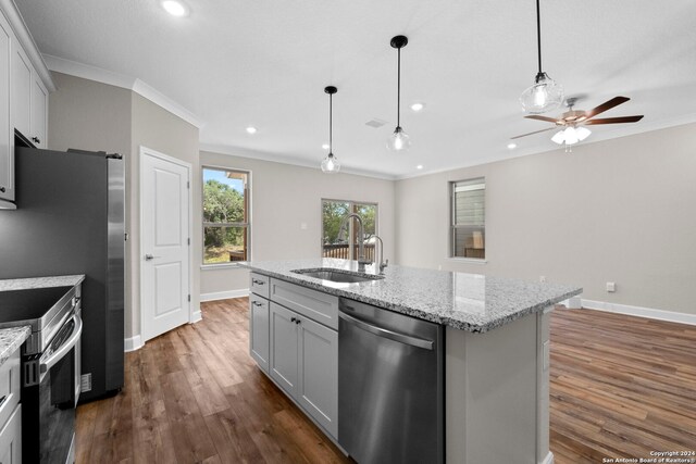 kitchen featuring appliances with stainless steel finishes, dark hardwood / wood-style flooring, light stone counters, a kitchen island with sink, and sink