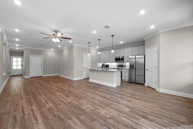 kitchen featuring pendant lighting, ornamental molding, an island with sink, appliances with stainless steel finishes, and wood-type flooring