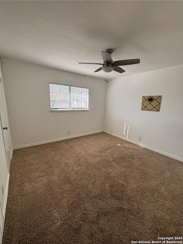 spare room featuring ceiling fan, dark carpet, and a textured ceiling