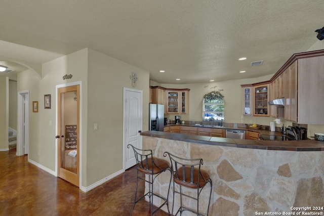 kitchen featuring sink, a kitchen breakfast bar, kitchen peninsula, a textured ceiling, and appliances with stainless steel finishes