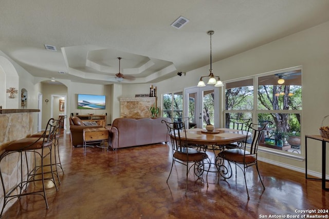 dining area featuring ceiling fan with notable chandelier, a raised ceiling, and french doors