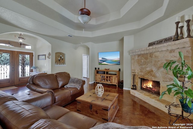 living room with a tray ceiling, a stone fireplace, and french doors