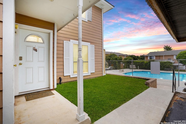 exterior entry at dusk with a fenced in pool, a patio area, and a lawn