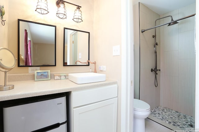 bathroom with tile patterned flooring, vanity, toilet, and tiled shower