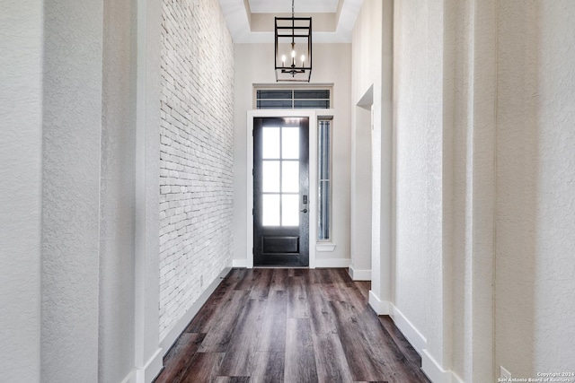 interior space with brick wall, a raised ceiling, dark wood-type flooring, a chandelier, and a high ceiling