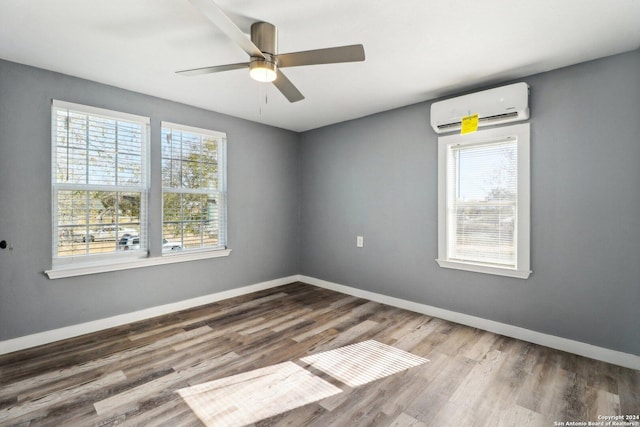 empty room with hardwood / wood-style flooring, an AC wall unit, ceiling fan, and a healthy amount of sunlight