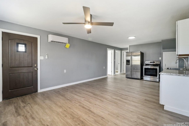 kitchen with stainless steel appliances, a wall unit AC, ceiling fan, sink, and white cabinets