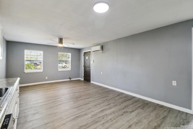 interior space featuring a wall mounted air conditioner, ceiling fan, and light wood-type flooring