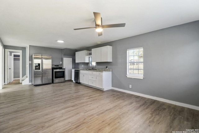 kitchen with light stone countertops, appliances with stainless steel finishes, ceiling fan, white cabinets, and light hardwood / wood-style floors