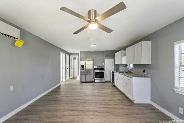 kitchen featuring a wall mounted air conditioner, appliances with stainless steel finishes, light stone countertops, sink, and white cabinets