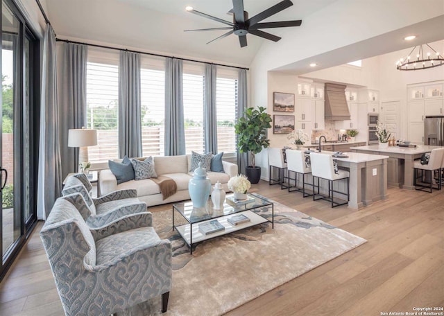 living room with ceiling fan with notable chandelier, light hardwood / wood-style floors, and lofted ceiling