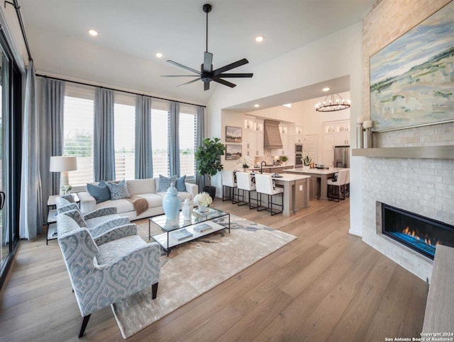 living room featuring ceiling fan with notable chandelier, lofted ceiling, a tile fireplace, and light hardwood / wood-style flooring