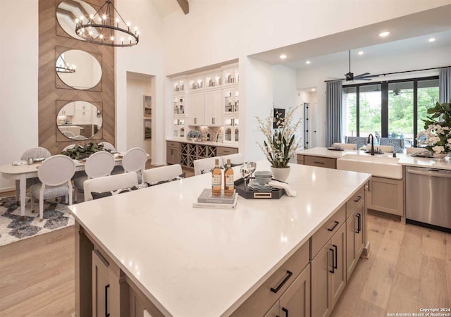 kitchen with stainless steel dishwasher, a spacious island, sink, decorative light fixtures, and light hardwood / wood-style flooring