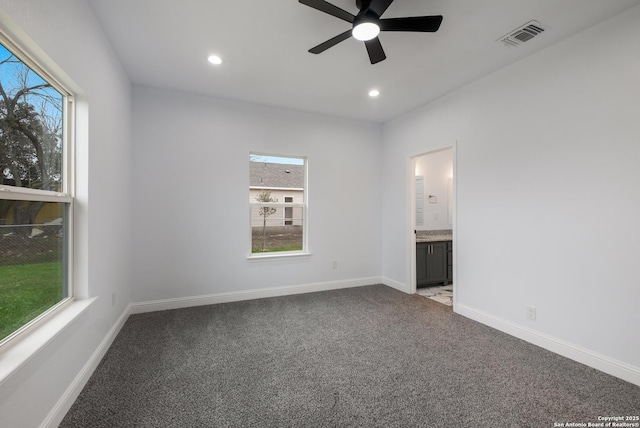 unfurnished bedroom with multiple windows, ensuite bathroom, carpet flooring, and ceiling fan