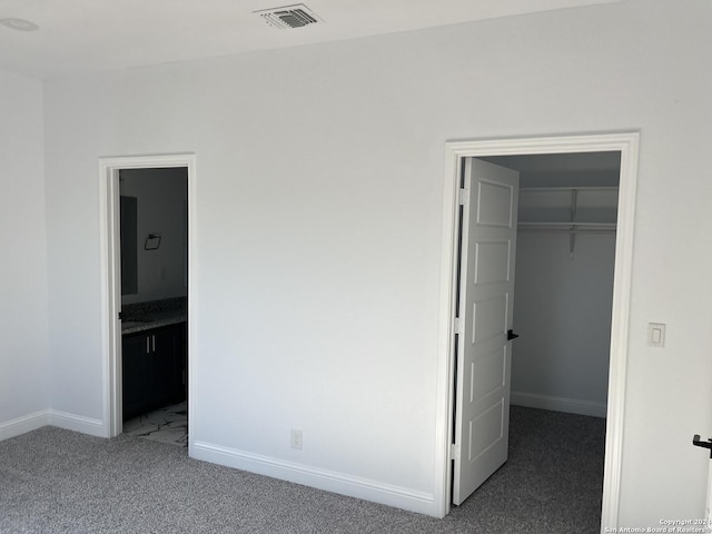 unfurnished bedroom featuring connected bathroom, dark carpet, a walk in closet, and a closet