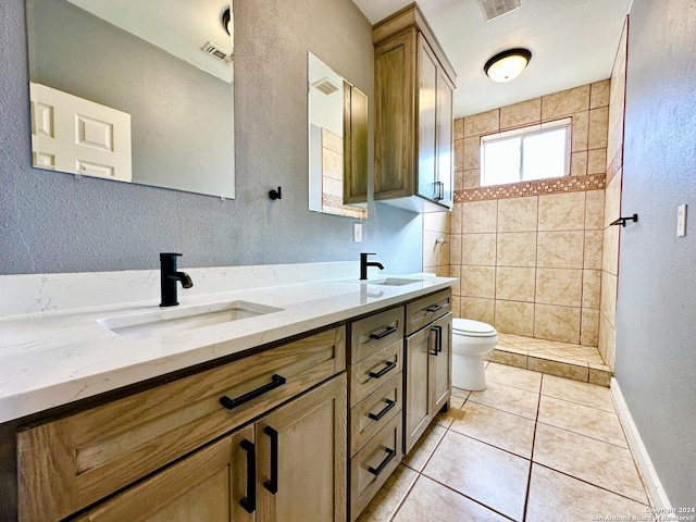 bathroom with tiled shower, tile patterned flooring, vanity, and toilet