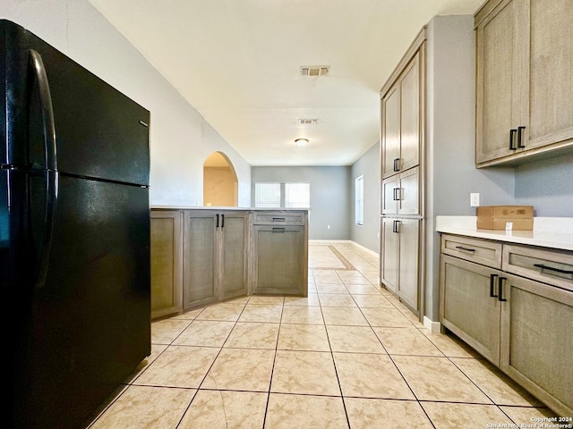 kitchen with black refrigerator, light tile patterned floors, and light brown cabinetry