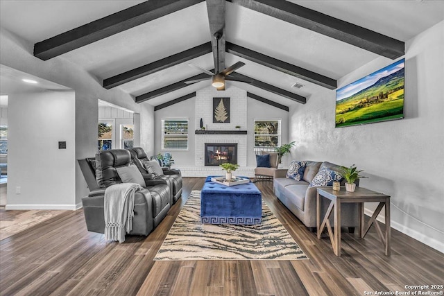 living room featuring ceiling fan, dark hardwood / wood-style floors, a brick fireplace, and vaulted ceiling with beams