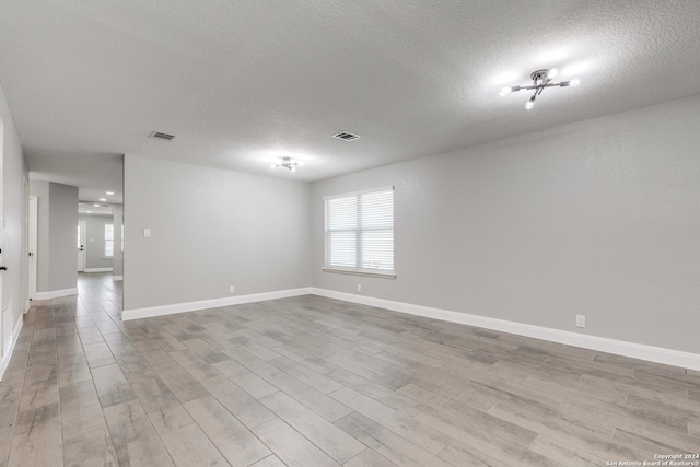 empty room with light wood-type flooring and a textured ceiling