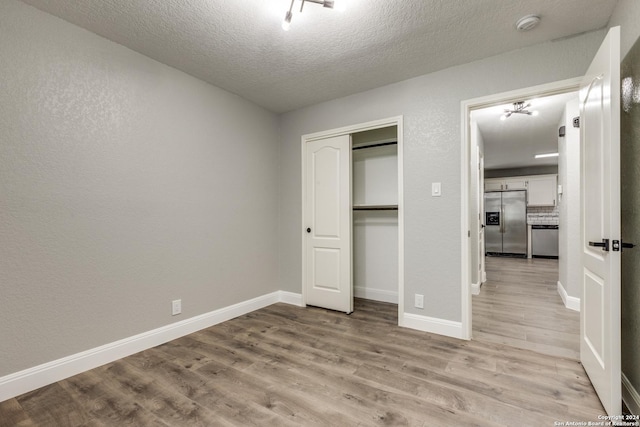 unfurnished bedroom with stainless steel fridge, light hardwood / wood-style floors, a textured ceiling, and a closet