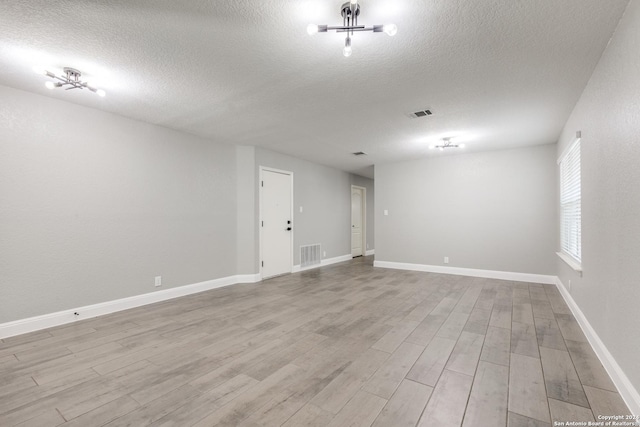 spare room featuring a notable chandelier, light wood-type flooring, and a textured ceiling