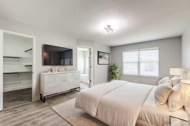 bedroom featuring a walk in closet, a textured ceiling, connected bathroom, and hardwood / wood-style flooring