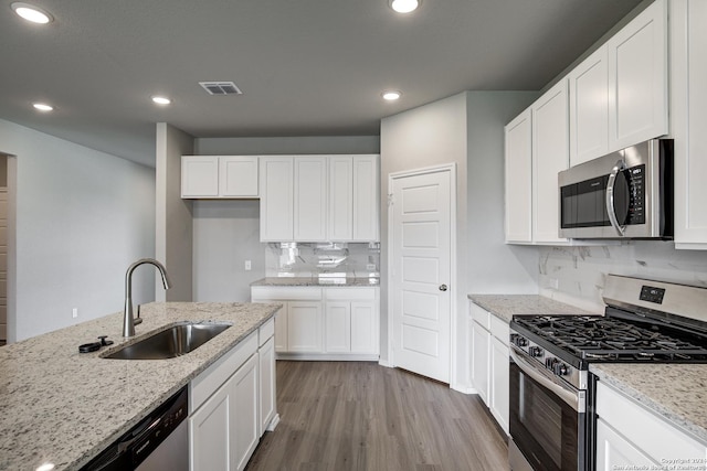 kitchen featuring appliances with stainless steel finishes, light wood-type flooring, light stone counters, sink, and white cabinetry