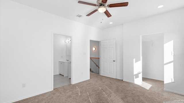 unfurnished bedroom featuring light carpet, ensuite bathroom, ceiling fan, a spacious closet, and a closet