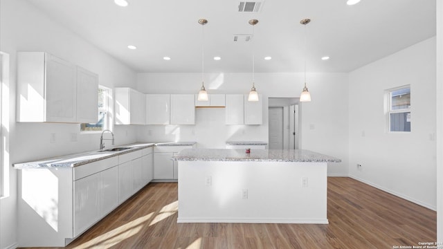 kitchen with a center island, sink, hardwood / wood-style flooring, decorative light fixtures, and white cabinetry