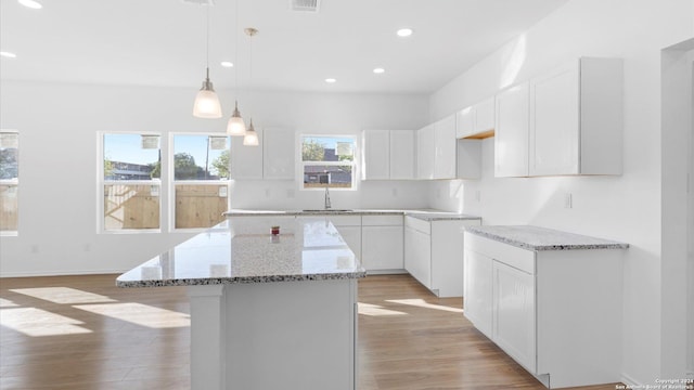 kitchen with white cabinetry, sink, hanging light fixtures, light hardwood / wood-style flooring, and a kitchen island