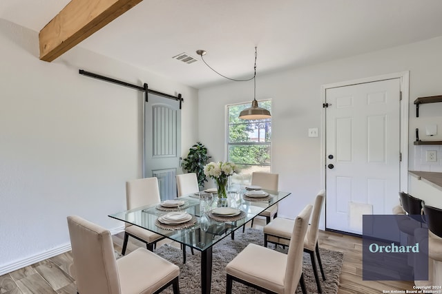 dining space featuring a barn door, beamed ceiling, and light wood-type flooring