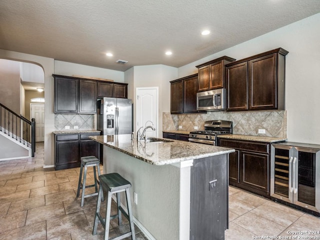 kitchen featuring sink, tasteful backsplash, wine cooler, a center island with sink, and appliances with stainless steel finishes