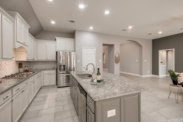 kitchen featuring light stone countertops, appliances with stainless steel finishes, tasteful backsplash, white cabinets, and an island with sink