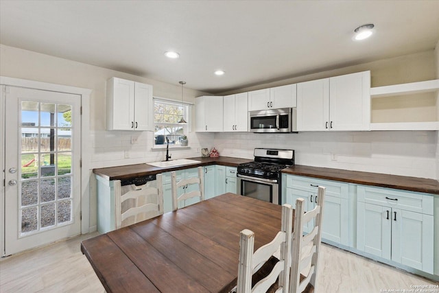 kitchen featuring stainless steel appliances, pendant lighting, white cabinets, and wooden counters