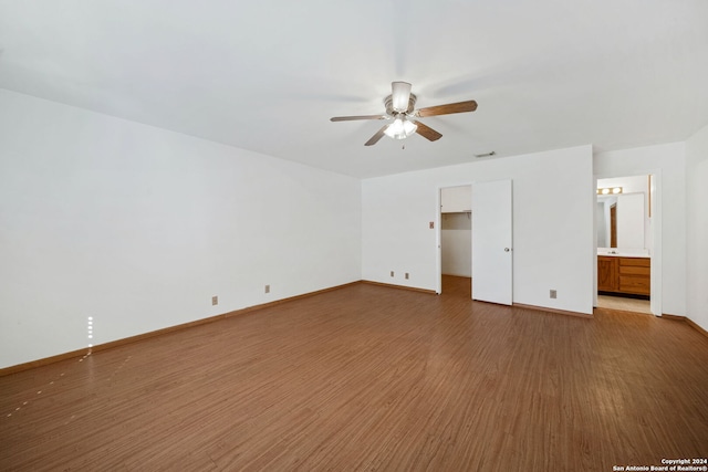 unfurnished bedroom featuring hardwood / wood-style floors, a walk in closet, ceiling fan, connected bathroom, and a closet