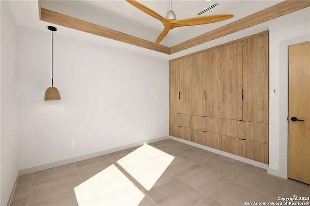 empty room with ceiling fan, a raised ceiling, and light tile patterned floors