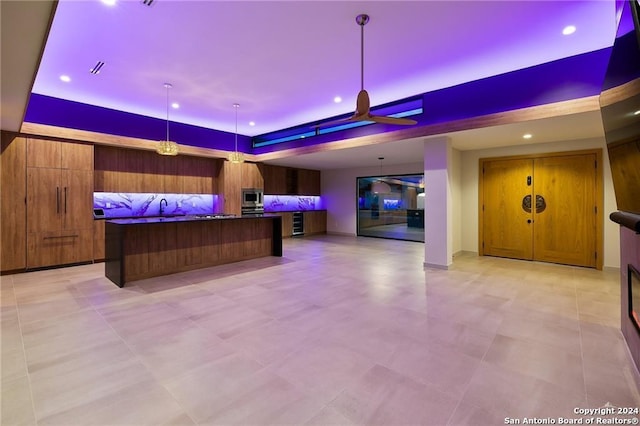 interior space with a raised ceiling, stainless steel microwave, hanging light fixtures, and sink