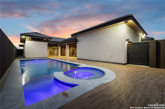 pool at dusk featuring an in ground hot tub