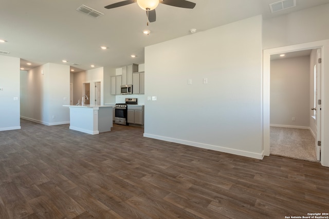 interior space featuring appliances with stainless steel finishes, gray cabinetry, ceiling fan, dark wood-type flooring, and an island with sink