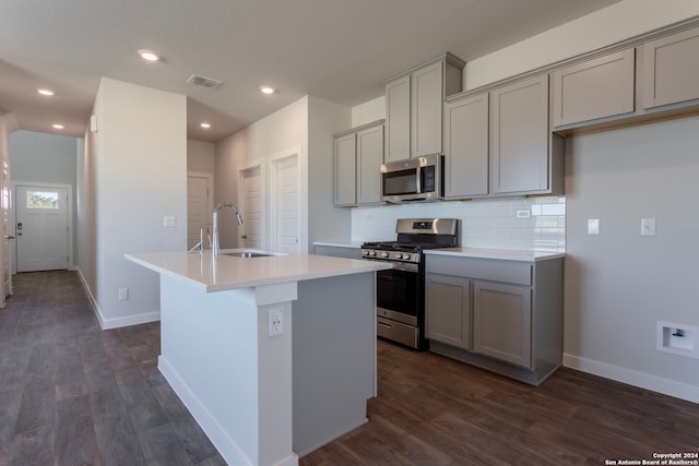 kitchen with backsplash, sink, stainless steel appliances, and a kitchen island with sink