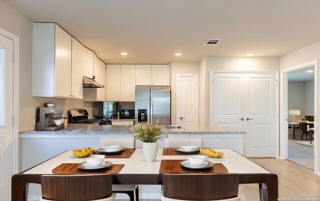 kitchen with stainless steel refrigerator with ice dispenser, light wood-type flooring, range with gas cooktop, sink, and white cabinetry