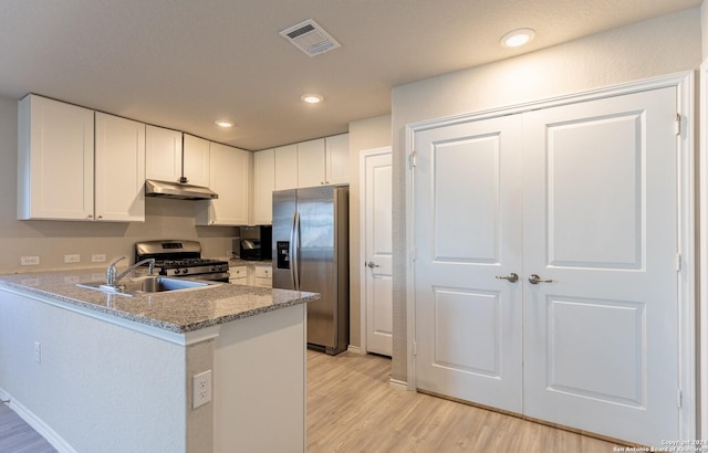 kitchen with kitchen peninsula, light stone counters, stainless steel appliances, sink, and white cabinetry