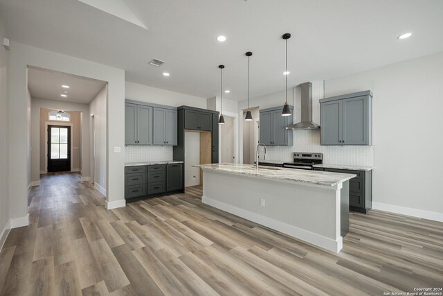 kitchen featuring wall chimney exhaust hood, decorative backsplash, stainless steel electric range oven, and a kitchen island with sink