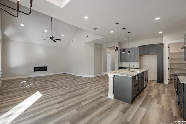 kitchen with pendant lighting, gray cabinetry, a center island with sink, sink, and light stone countertops