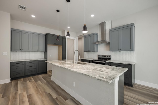 kitchen with electric range, sink, wall chimney exhaust hood, light stone countertops, and a center island with sink